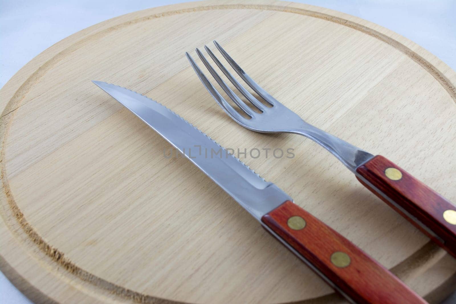 Fork and knife with red wooden handle on a plate of natural wood.