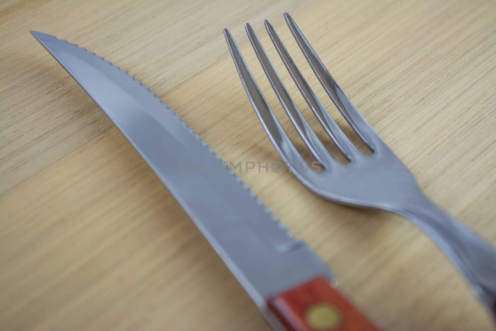 Fork and knife with red wooden handle on a plate of natural wood.