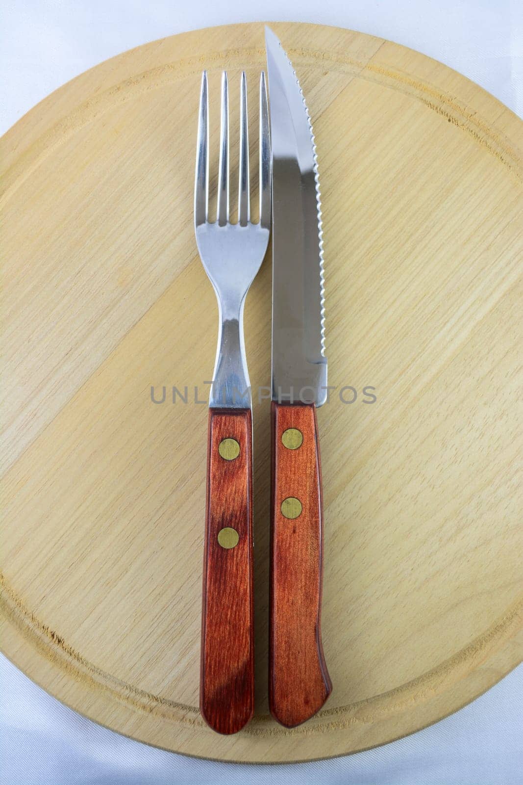 Fork and knife with red wooden handle on a plate of natural wood.