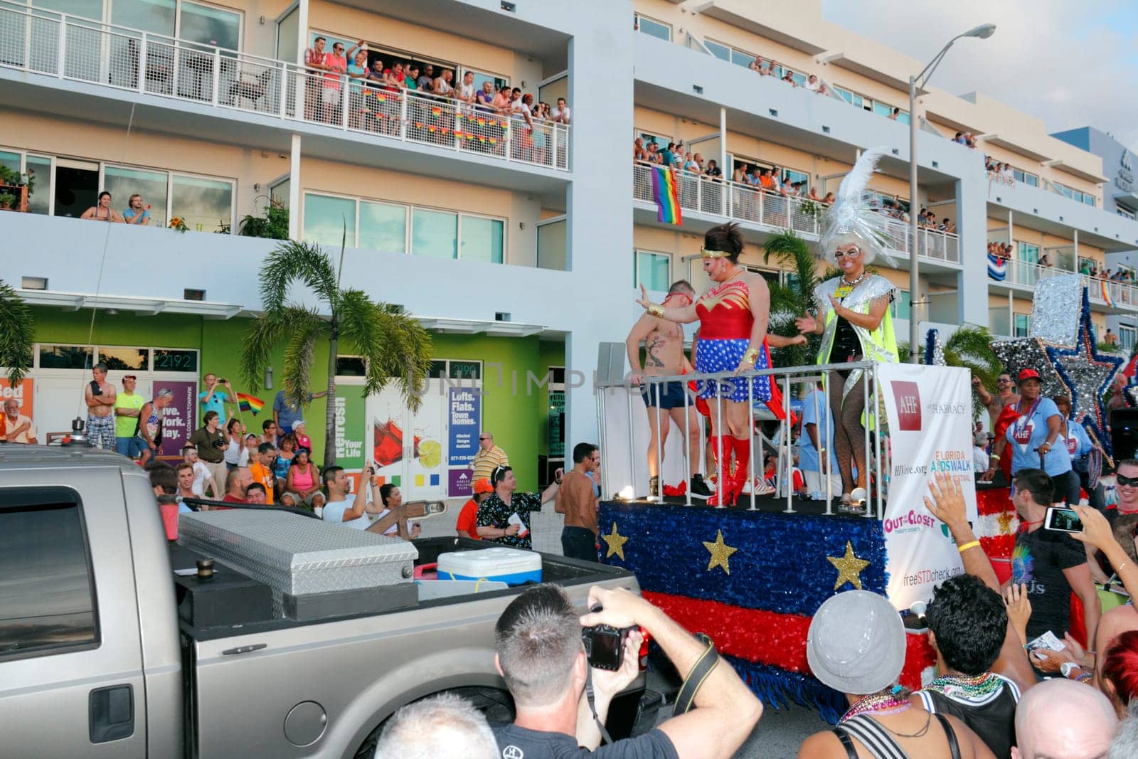 WILTON MANORS, FLORIDA - JUNE 22, 2013: Large patriotically decorated gay parade AHF or Aids Healthcare Foundation float with two feminine performers in front, various other people and signs in back.
