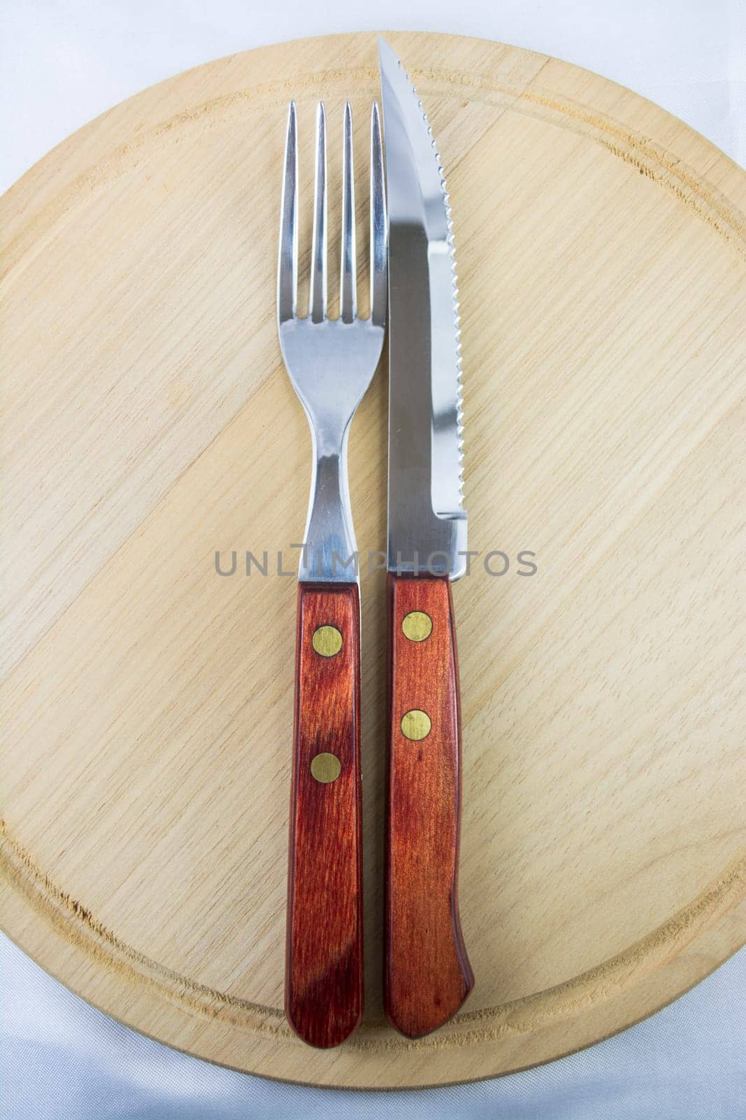 Fork and knife with red wooden handle on a plate of natural wood.