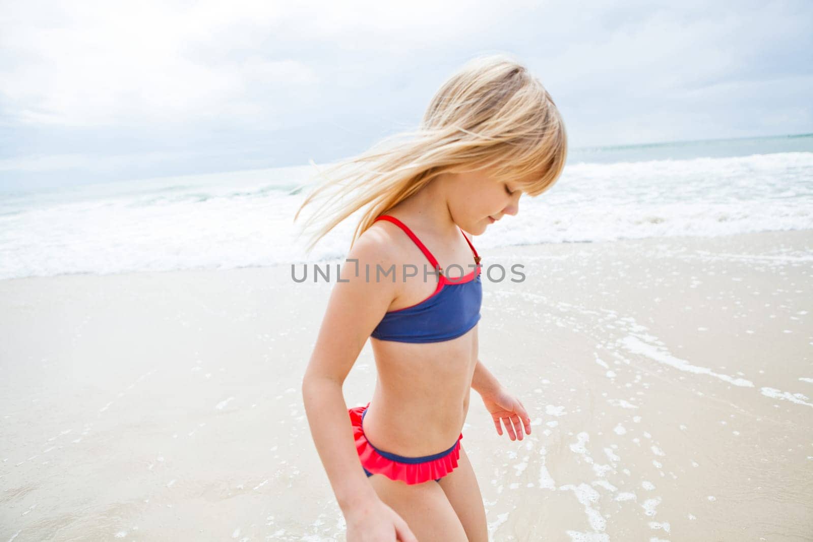 Happy cute young girl standing in water at beach on sunny day