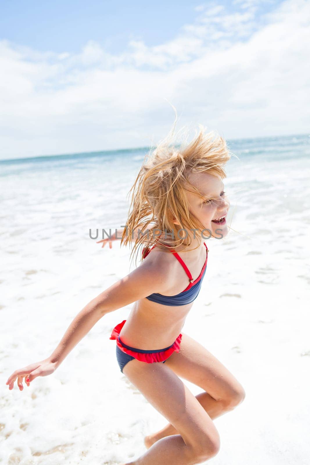 Smiling cute young girl jumping and having fun at beach on sunny day