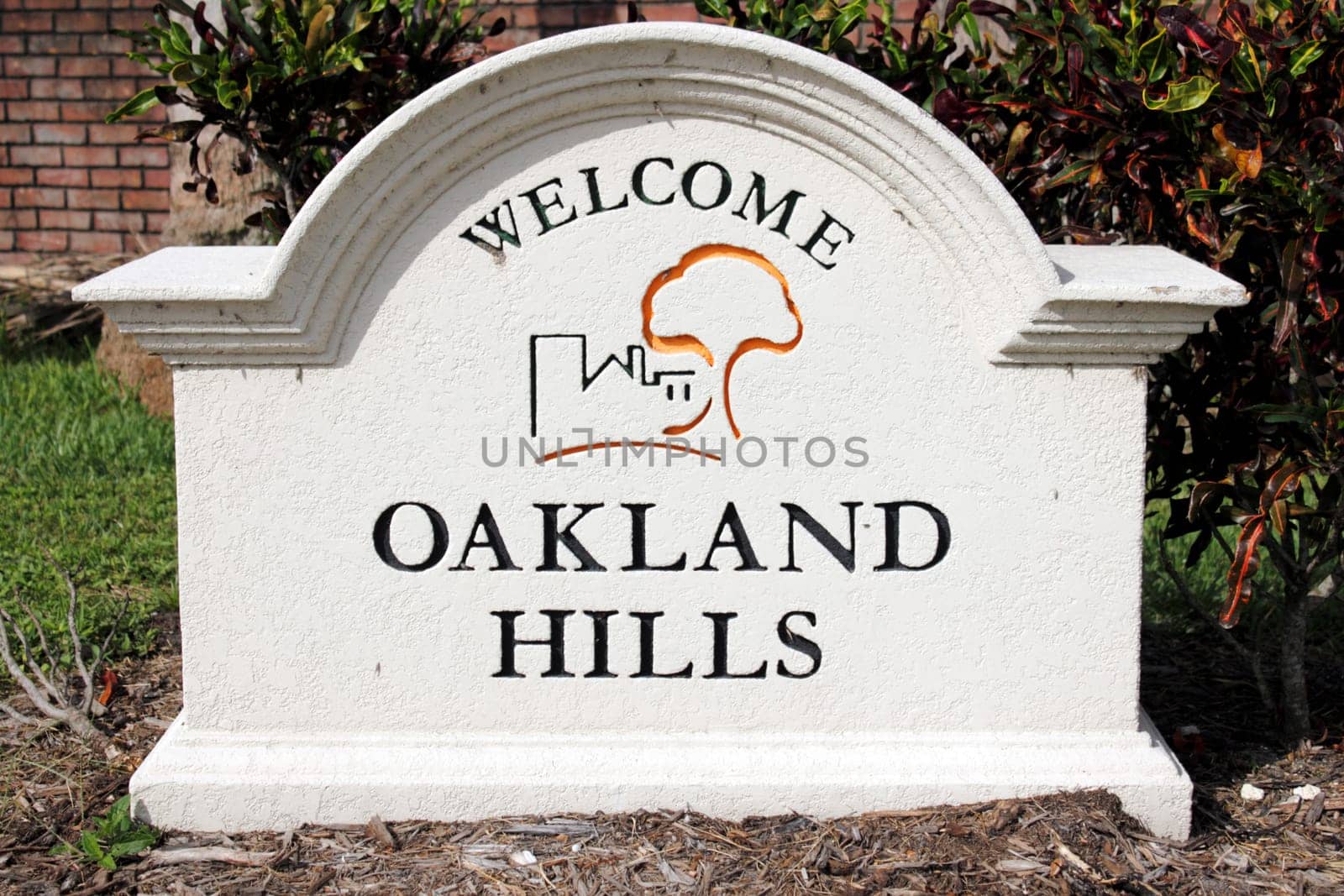 OAKLAND PARK, FLORIDA - JULY 1, 2013:  Painted cement Oakland Hills Welcome sign with graphic seen closeup outside on a sunny day with tropical foliage and a brick wall behind it.