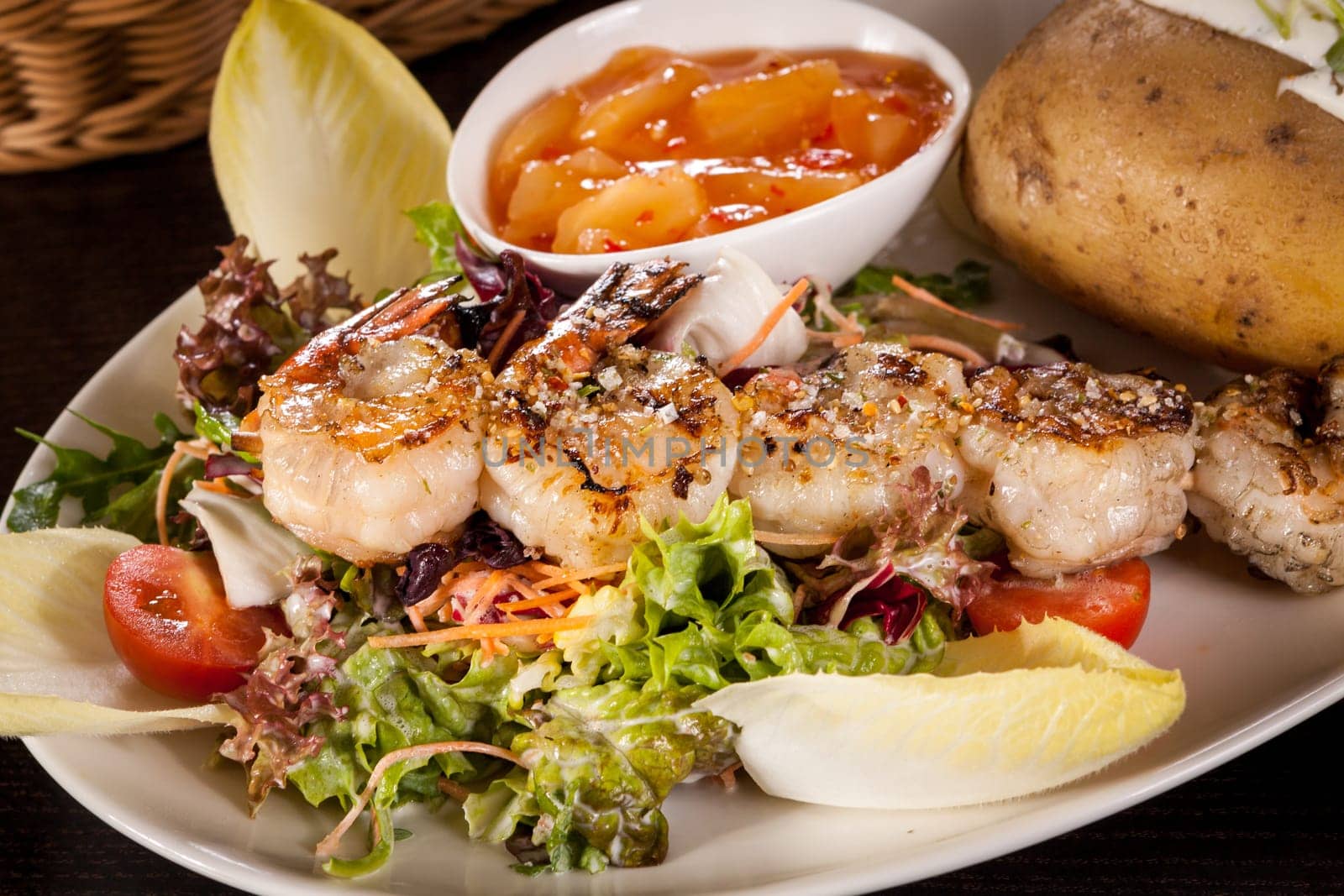 Roasted shrimp on a skewer on a mixed salad with dipp and foil potato on a plate