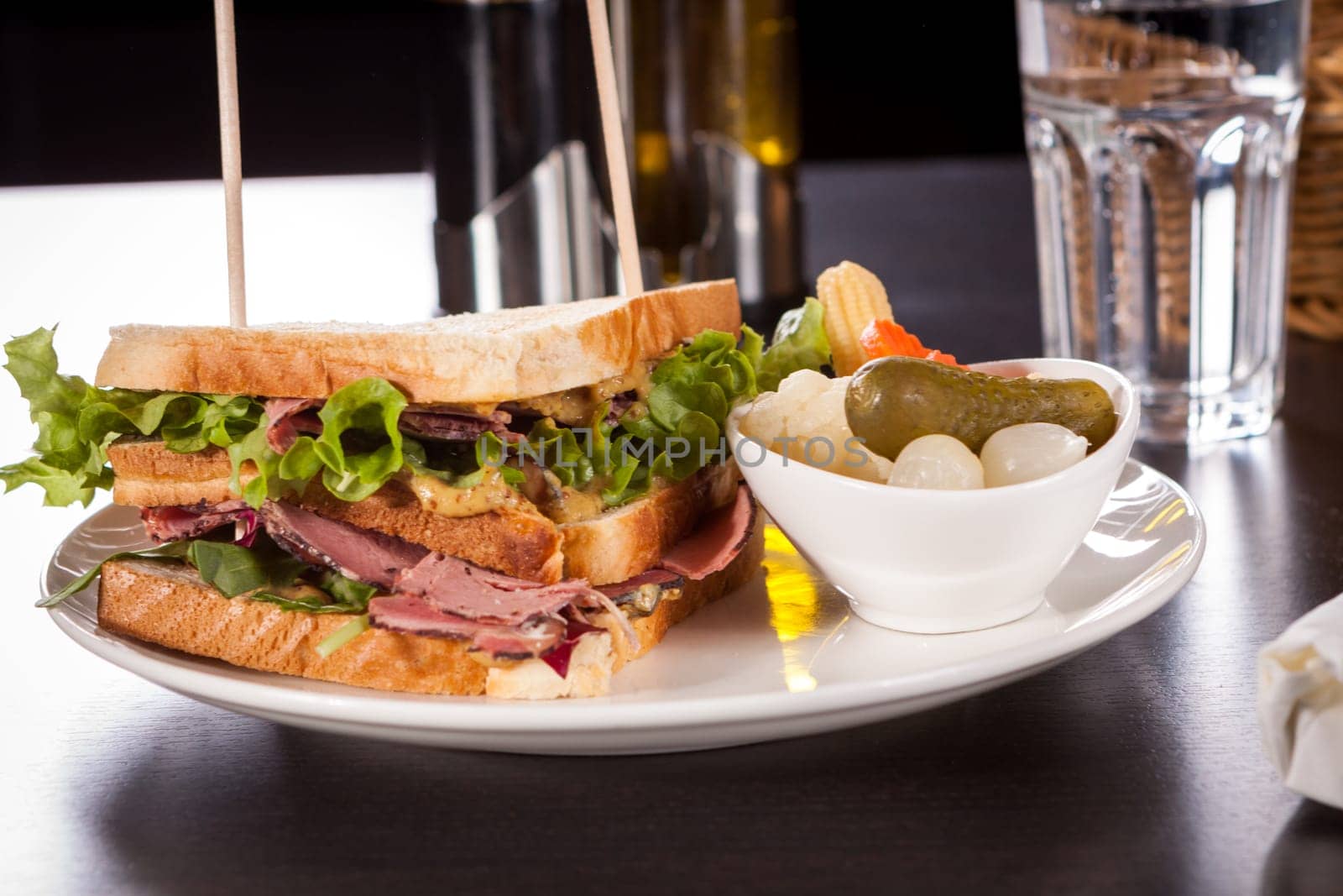 Delicious sandwich clubsandwich with bacon ham cheese and one with mixed pickels on a plate