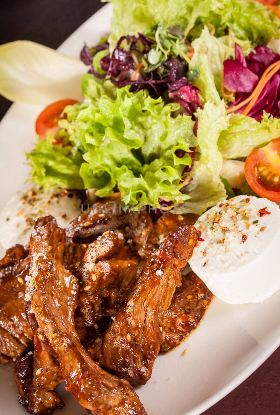 Fresh salad with fresh goat cheese and fried beef strips served on a plate