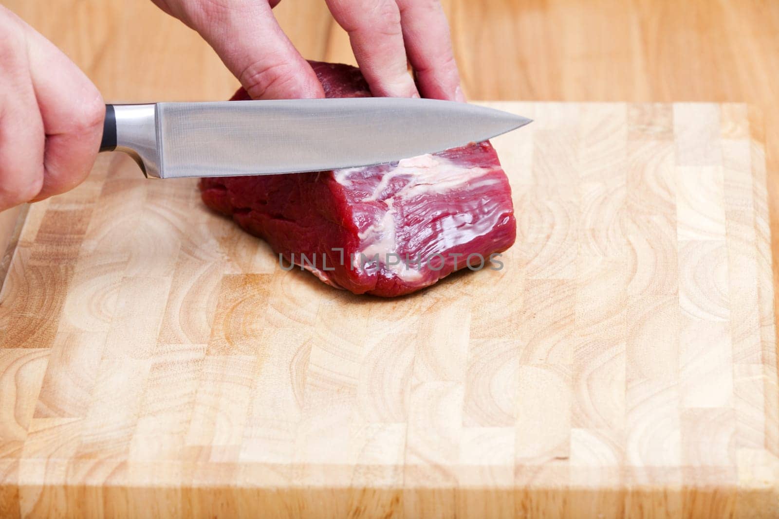 Piece of raw beef fillet is processed with a knife