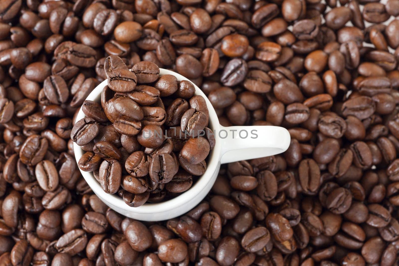 Espresso cup stands between many coffee beans
