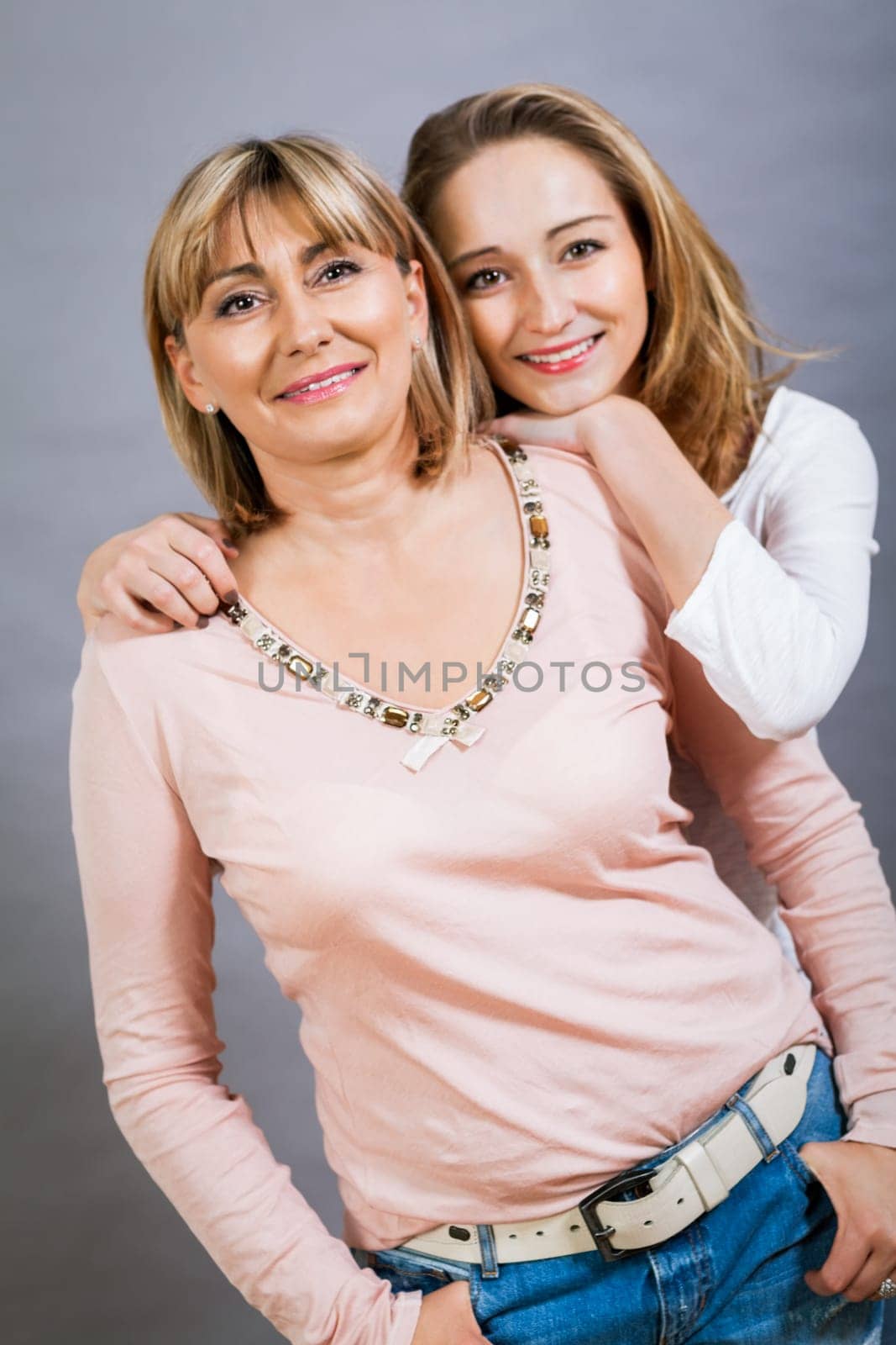 Attractive adult wife mother with teen daughter portrait against grey background family genration