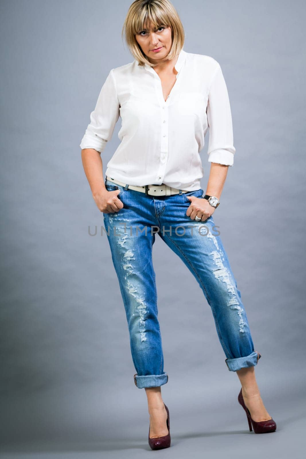 adult blonde attractive woman with blue jeans and white blouse against grey background fashion trendy