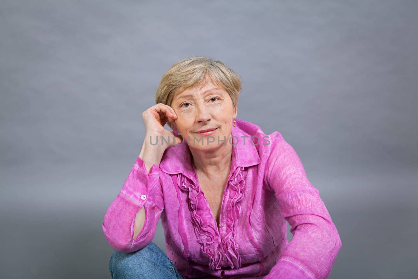 happy older woman seniorwith light hair and fold with pink blouse against grey background healthy