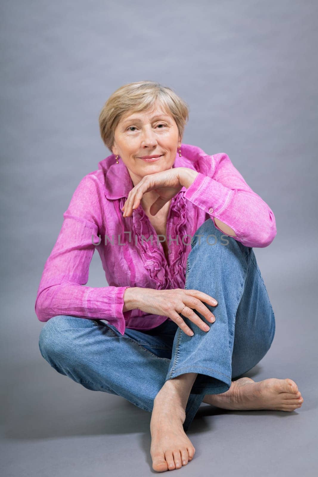happy older woman seniorwith light hair and fold with pink blouse against grey background healthy