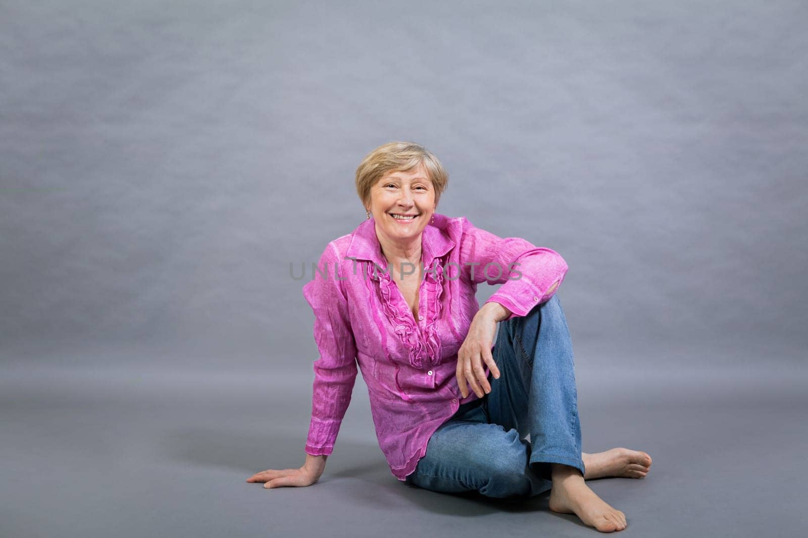 happy older woman seniorwith light hair and fold with pink blouse against grey background healthy