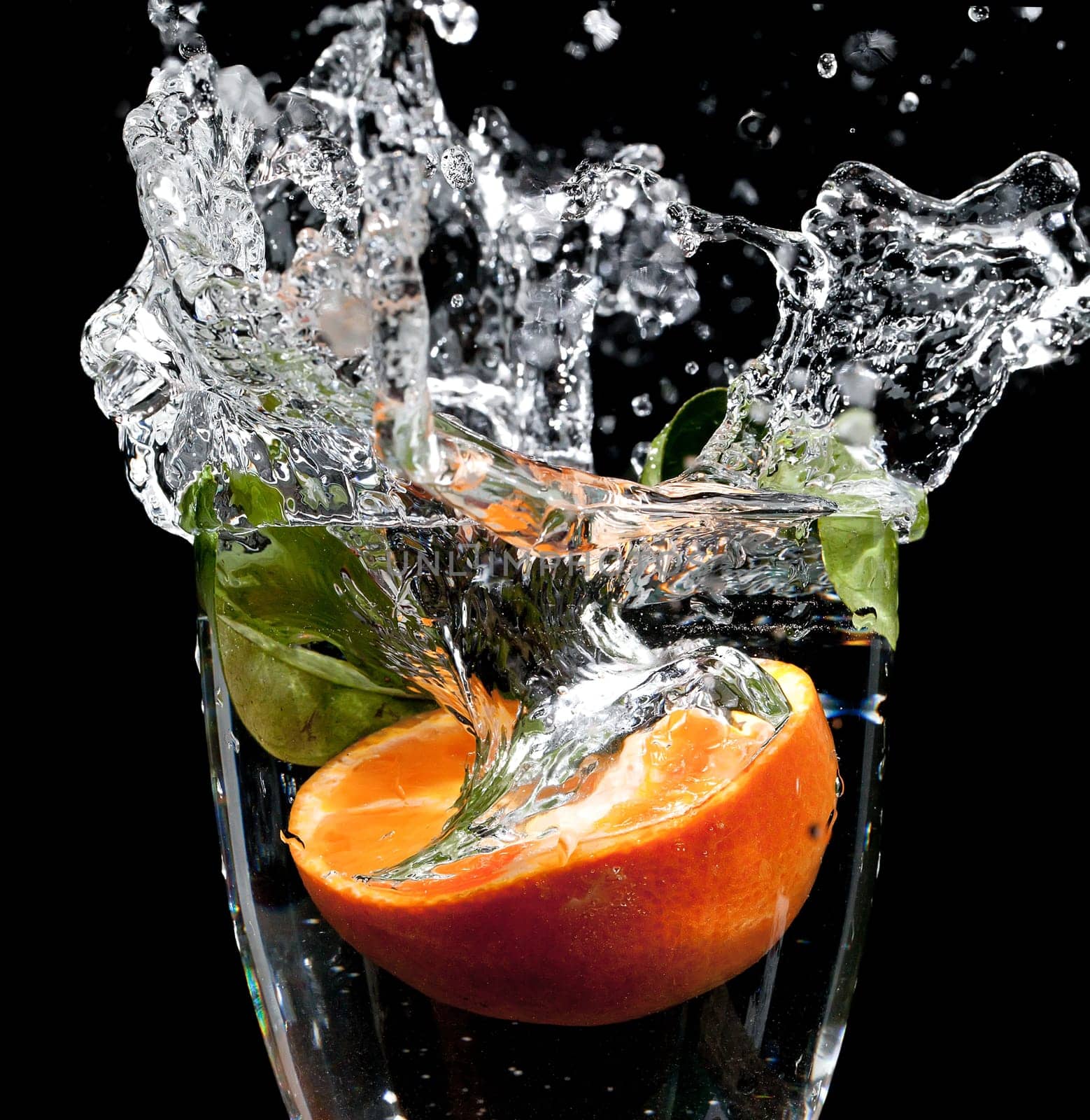 Orange dropped into a glass of water with big splash frozen in time, on a black background
