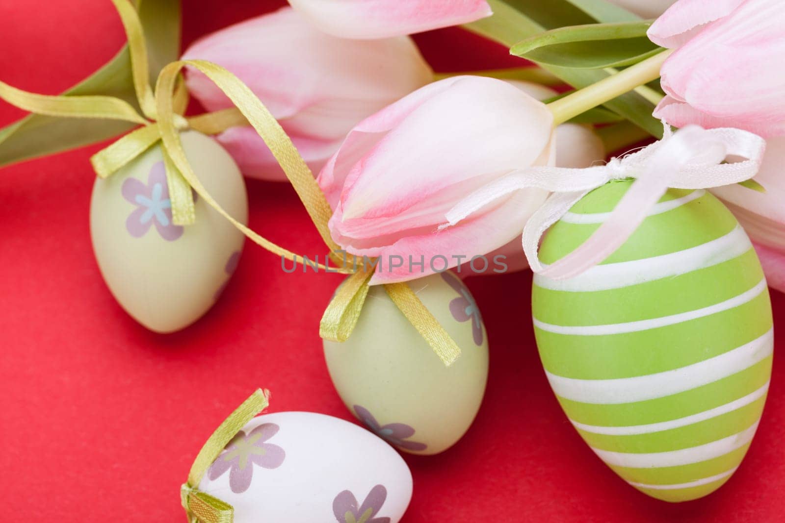 pink tulips decorated with easter eggs as a close-up with text space on a red background