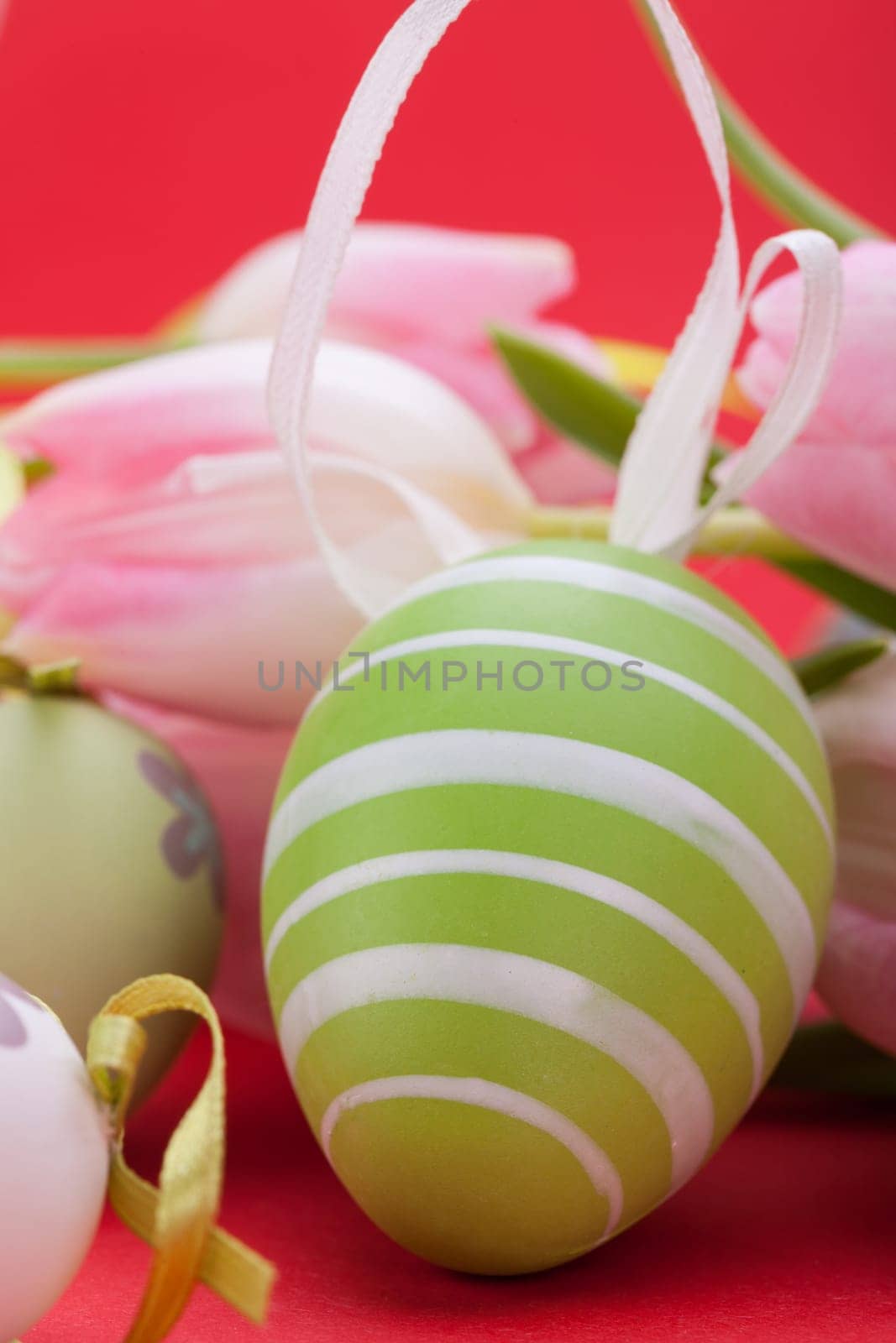 pink tulips decorated with easter eggs as a close-up with text space on a red background