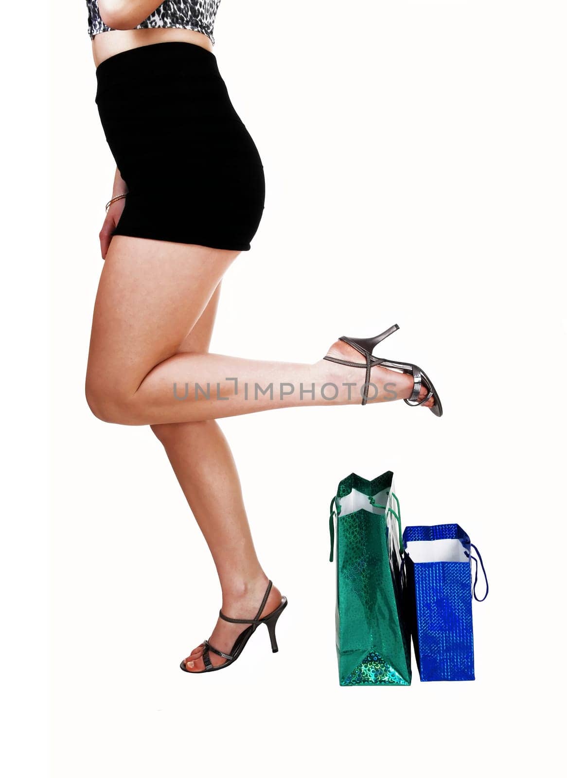 A lovely young woman's bottom body part in a black skirt holding her leg up,  .with shopping bags on floor for white background..