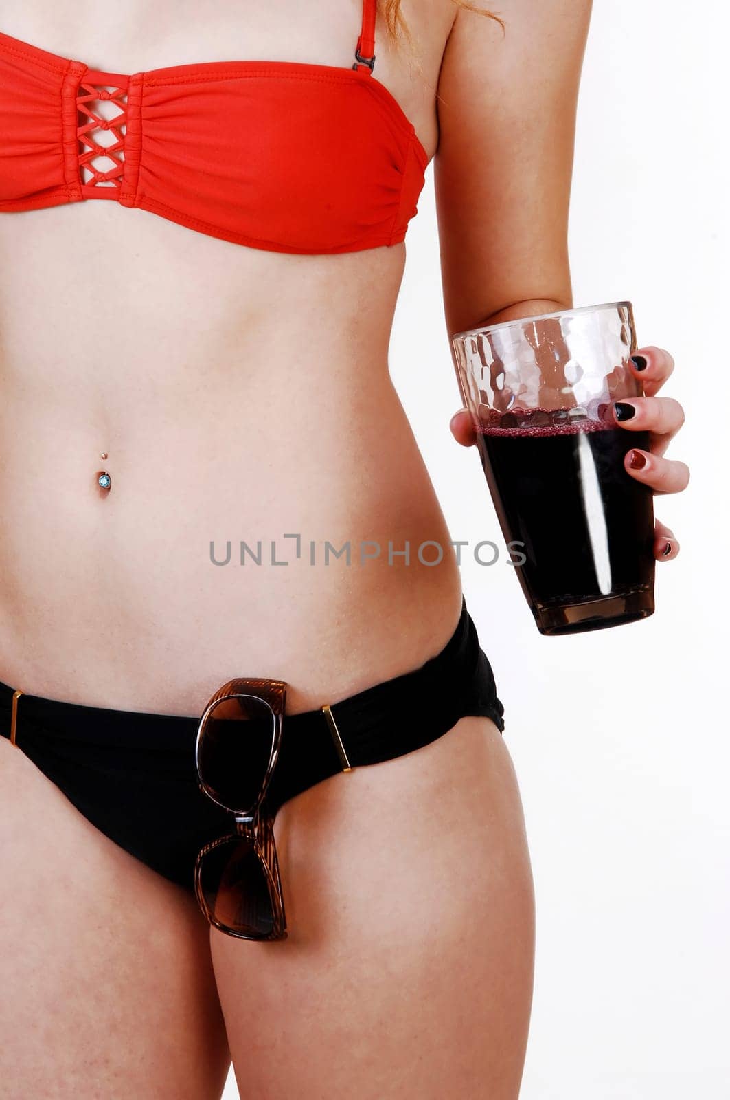 A lovely young slim halve woman in a red bikini top and black bottom standing.for white background holding a drink in her hands..