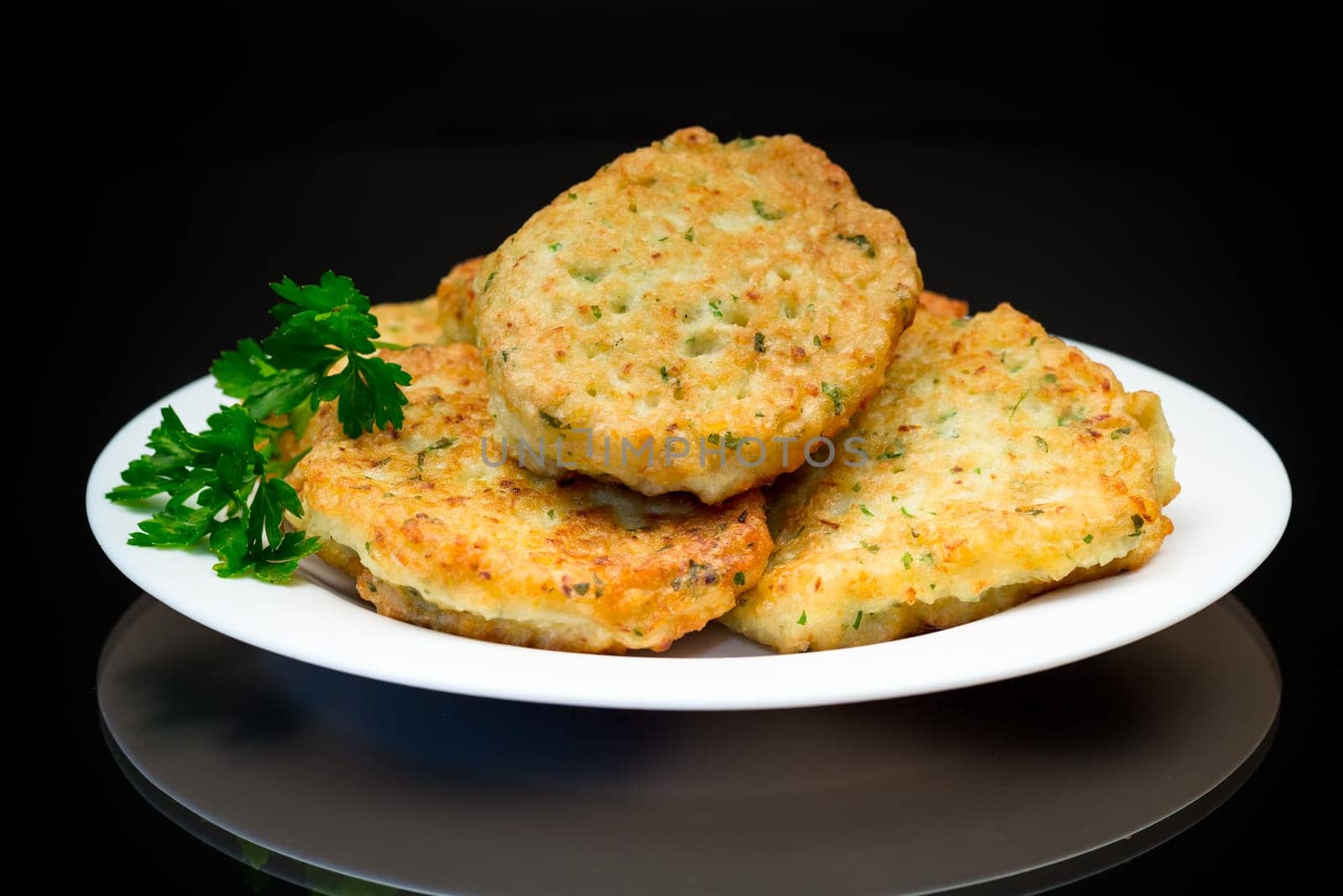 cooked fried potato cutlets with herbs, in a plate isolated on a black background.