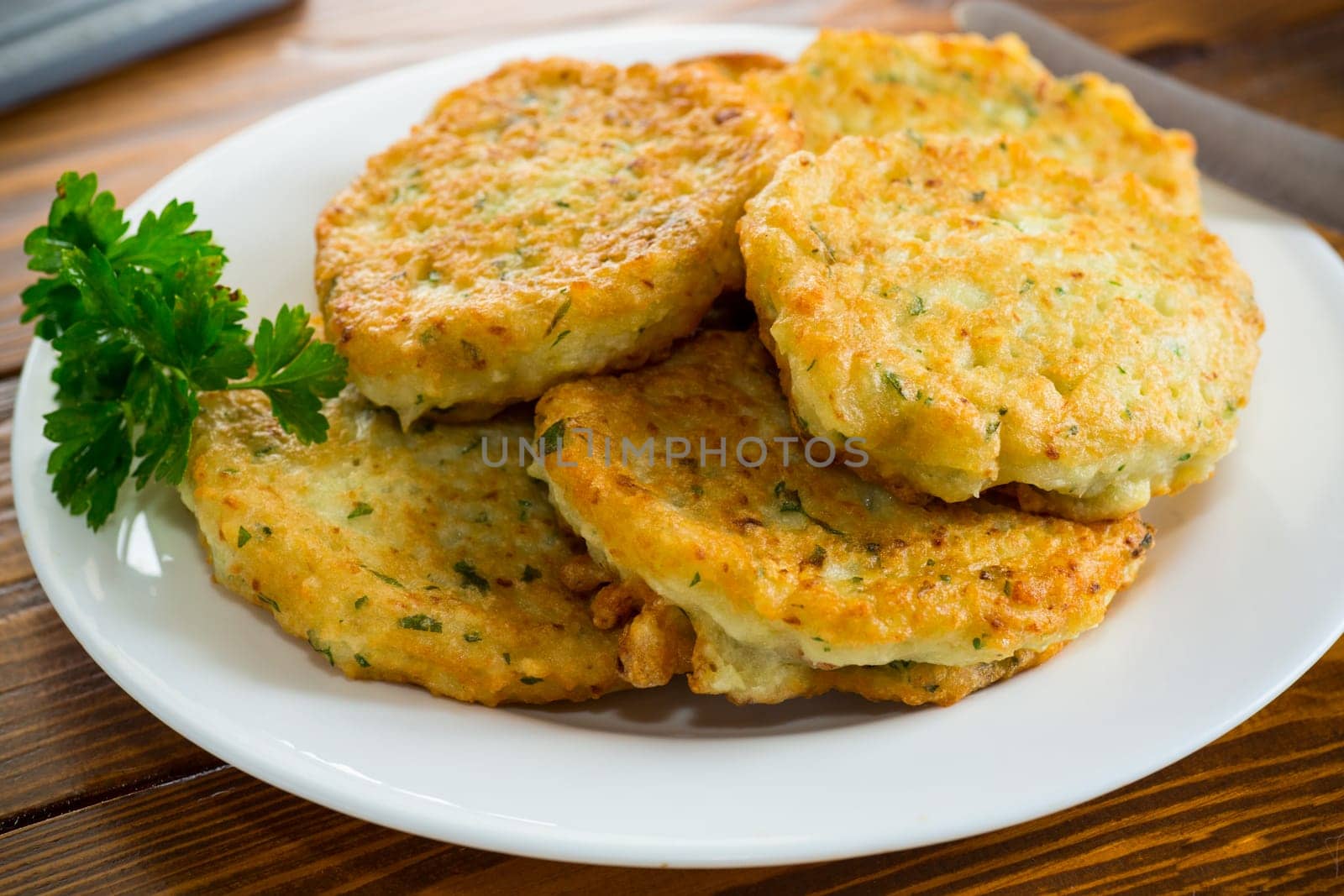 cooked fried potato cutlets with herbs, in a plate on a wooden table.