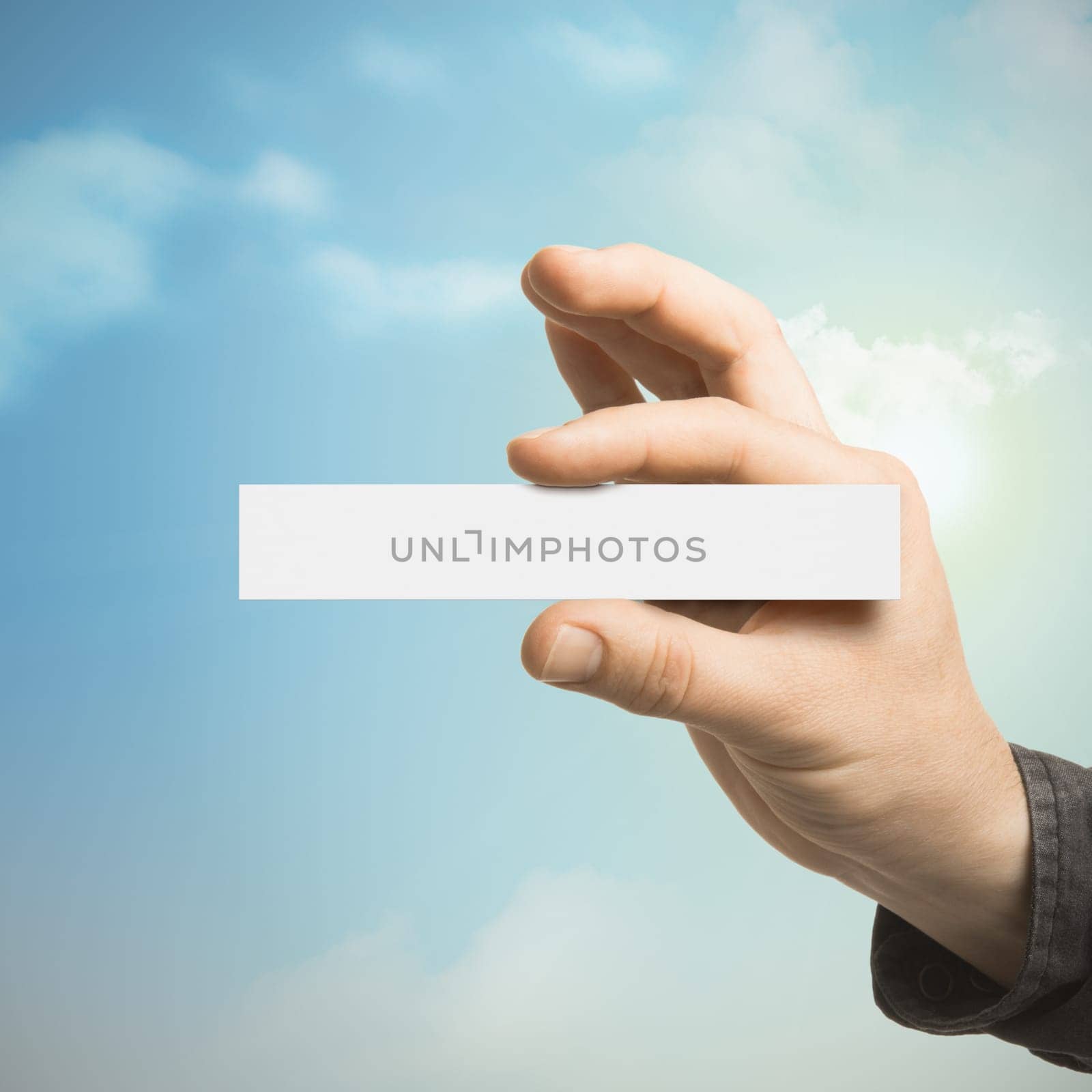 One hand holding a blank card with a blue sky at the background with clouds and sun. Communication concept for Business or Marketing