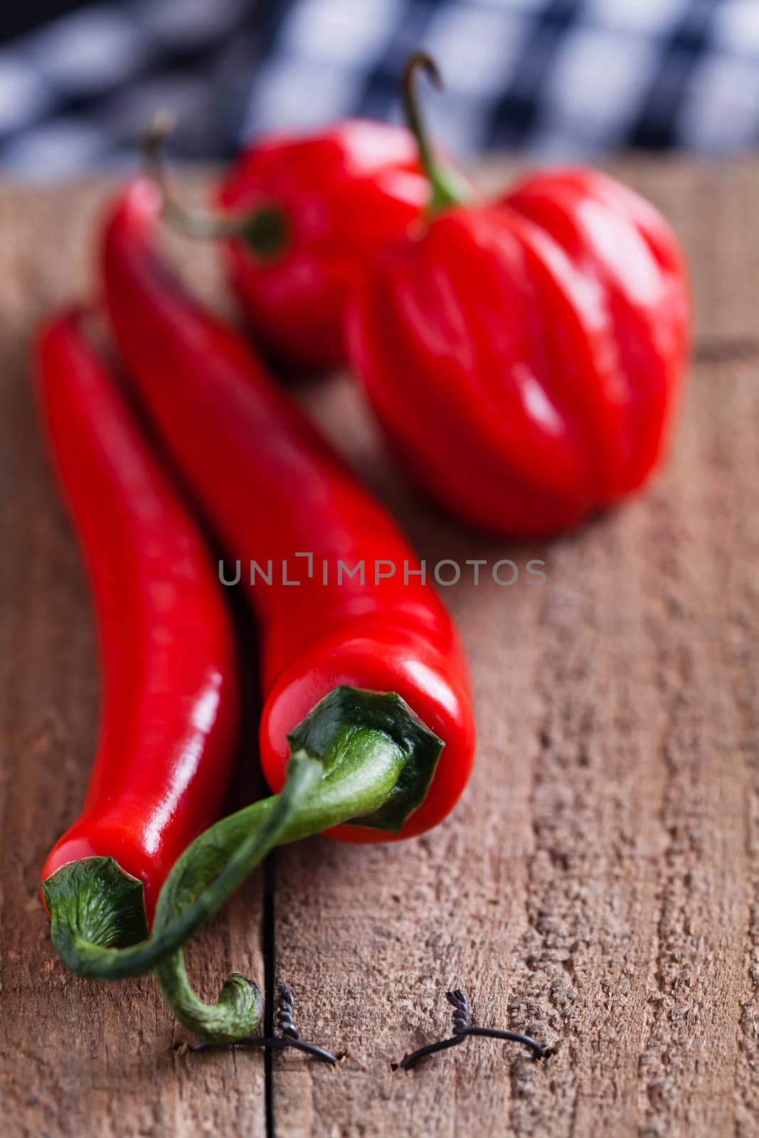 Closeup of long and round red chili peppers resting on wooden board surface