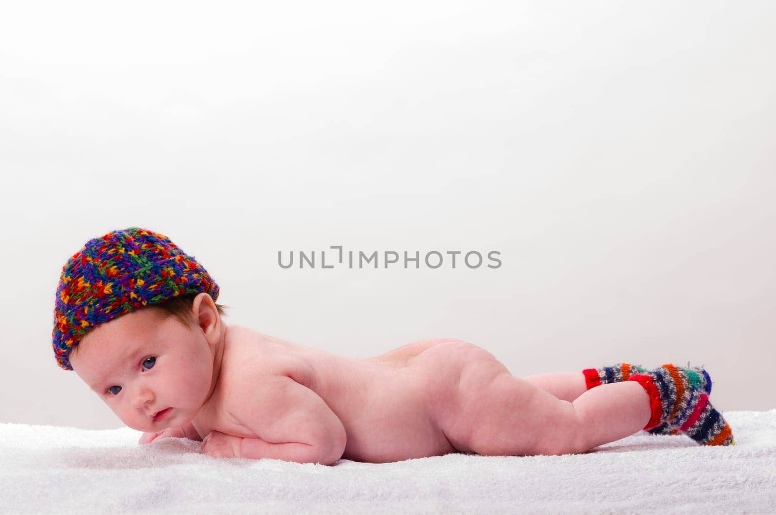 Sweet newborn baby wearing a colorful woolen cap and smiling, isolated against a white background.