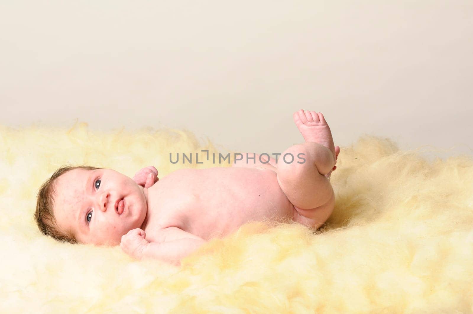 A little newborn baby lies on a sheepskin.