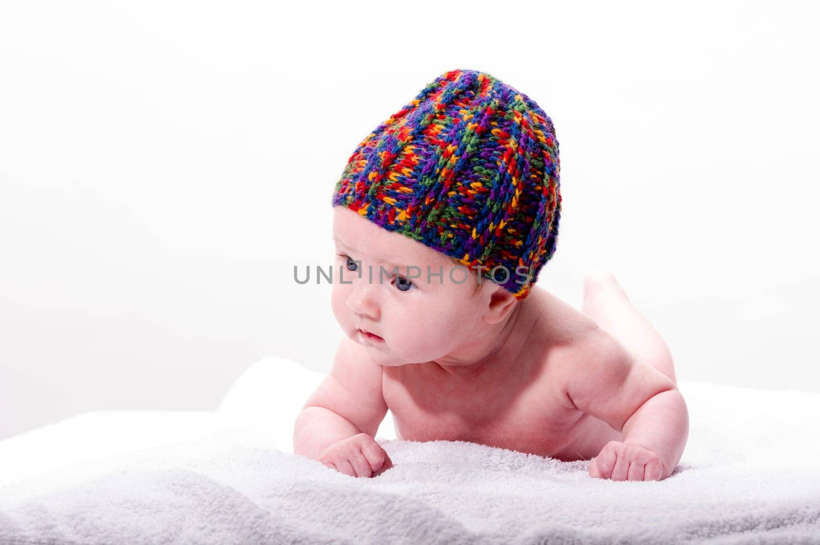 Sweet newborn baby wearing a colorful woolen cap and smiling, isolated against a white background.
