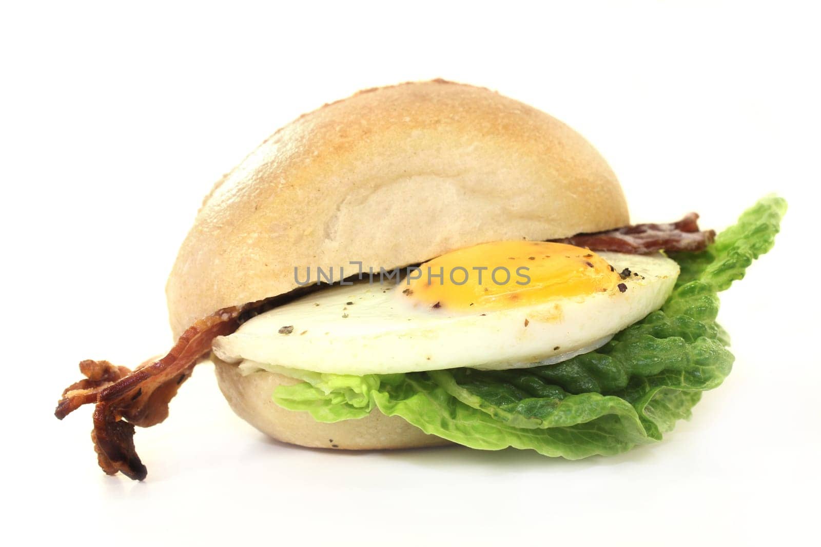 a bun covered with fried egg,bacon and salad