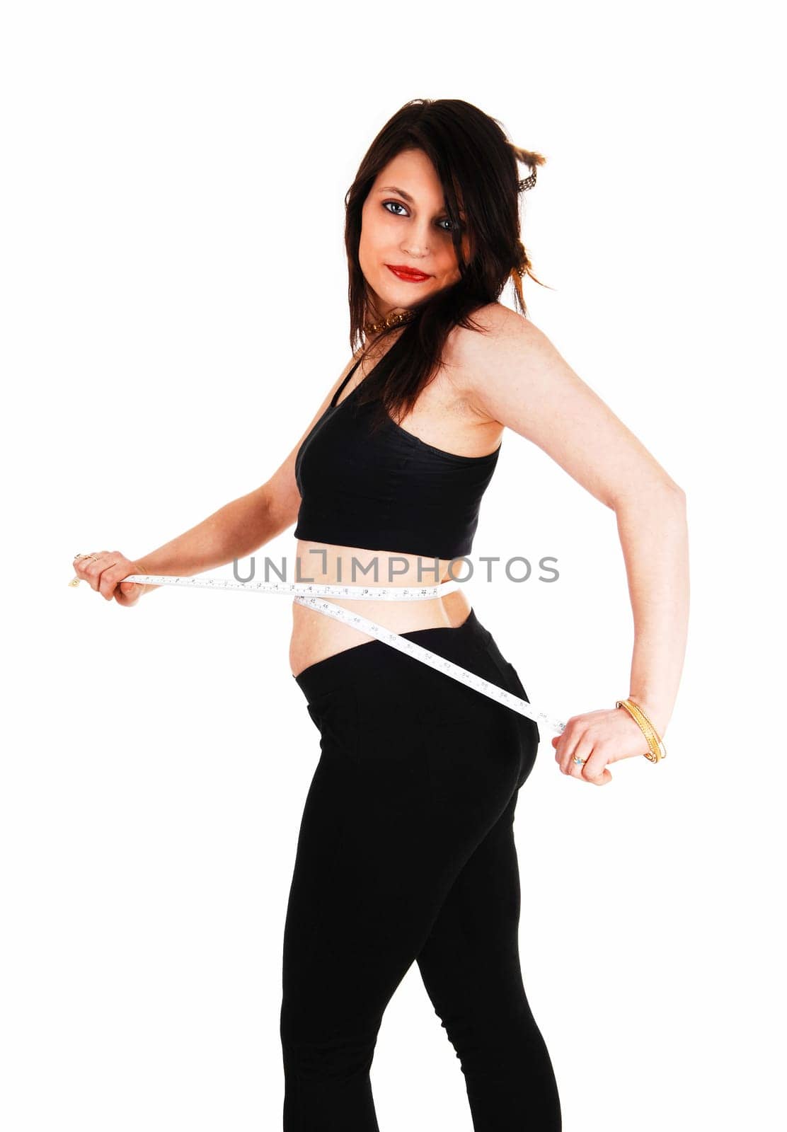 A young woman in black tights and top taking her measurements with a.tape for white background..