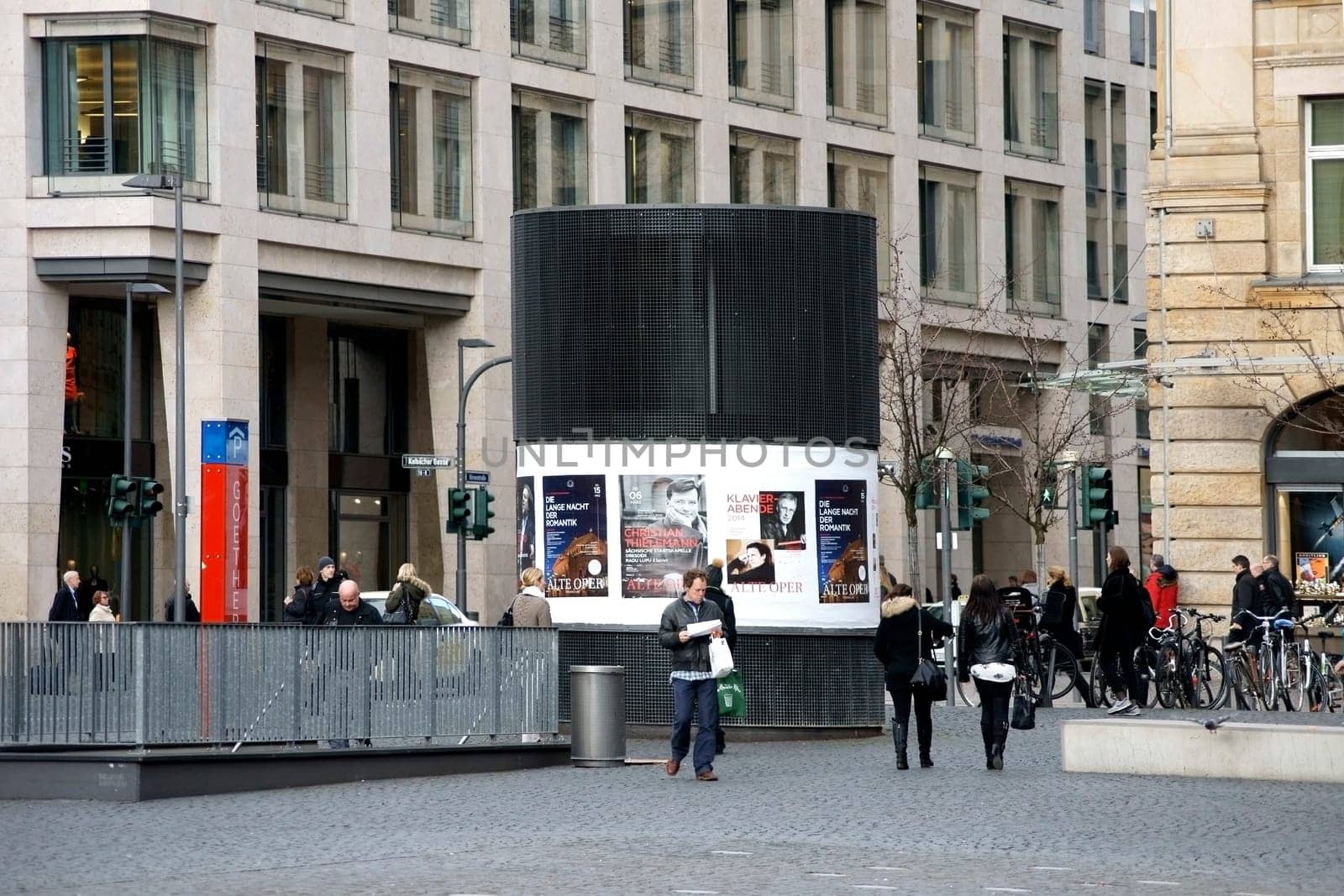 Frankfurt,Germany – February 19,2014: The Goetheparklplatz car park entrance with a lithograph column covered with posters and passers-by on February 19,2014 in Frankfurt.
