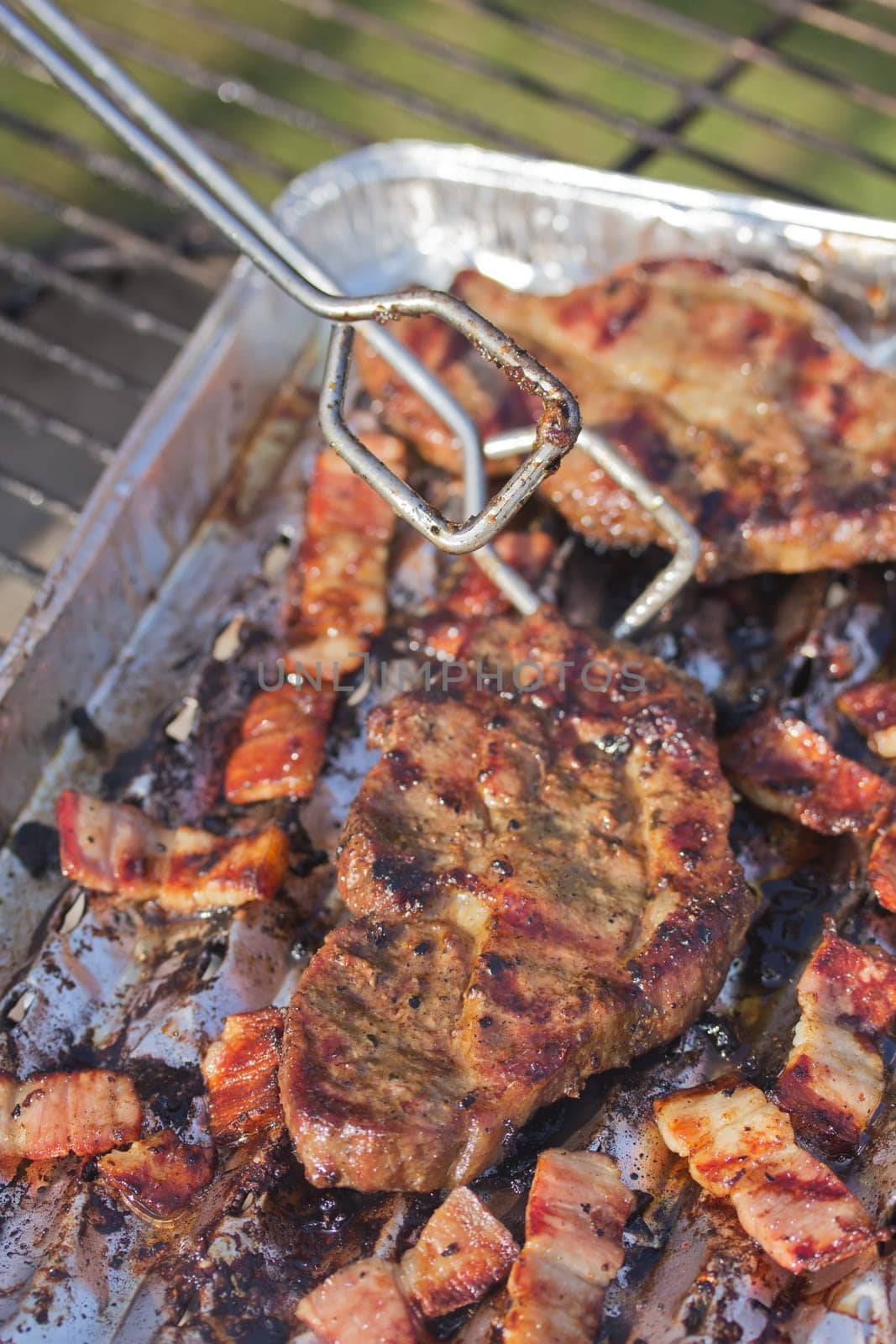 Grilled steak and bacon on an aluminum tray, which prevents dripping fat into the fire.