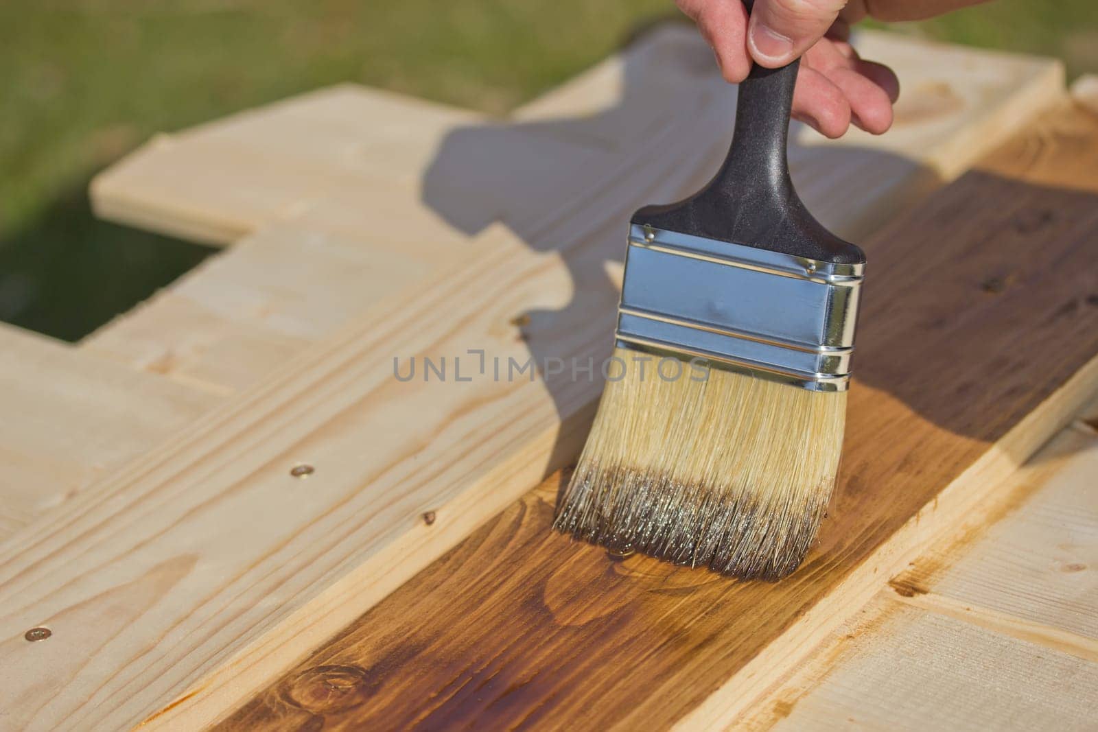A man is painting with brush a wooden board.