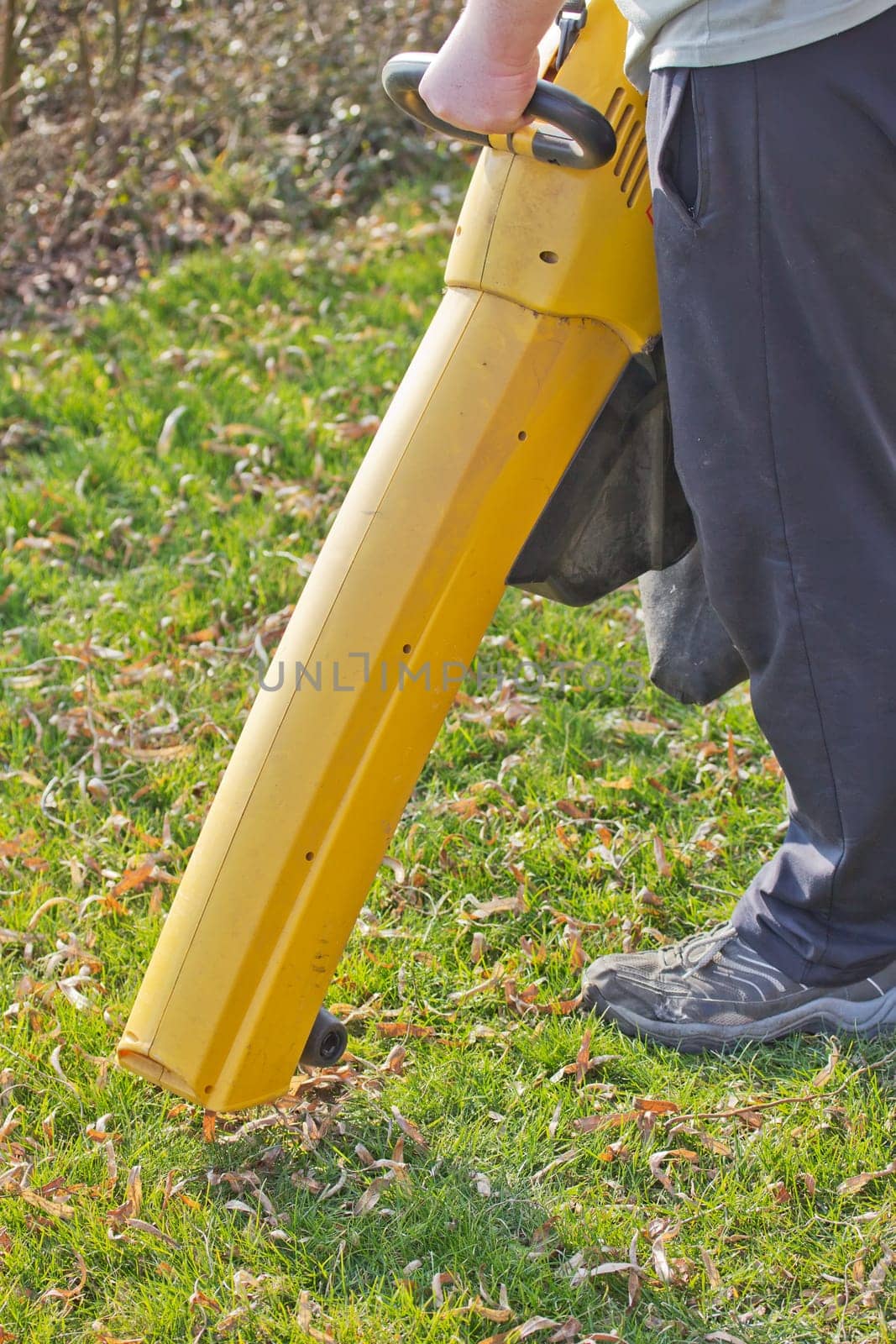 Man is sapping by yellow electric leaf vacuum outside.