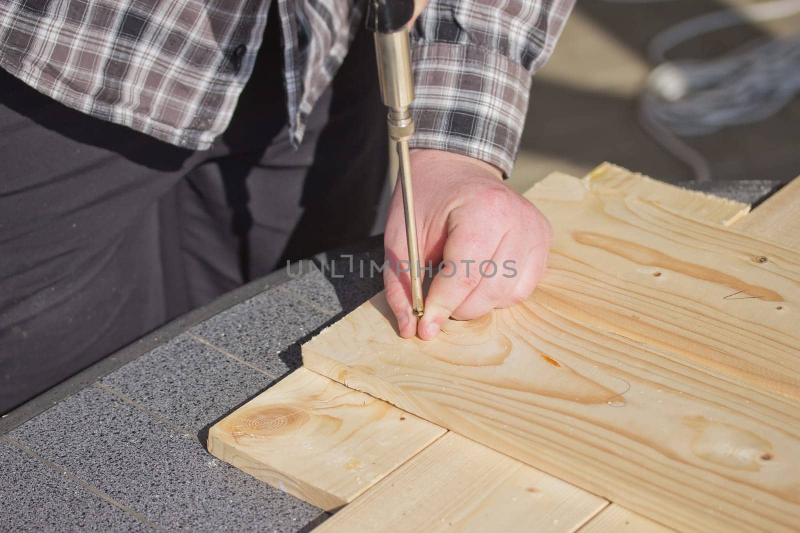 Man in a plaid shirt is bolting  screwed into a wooden board.
