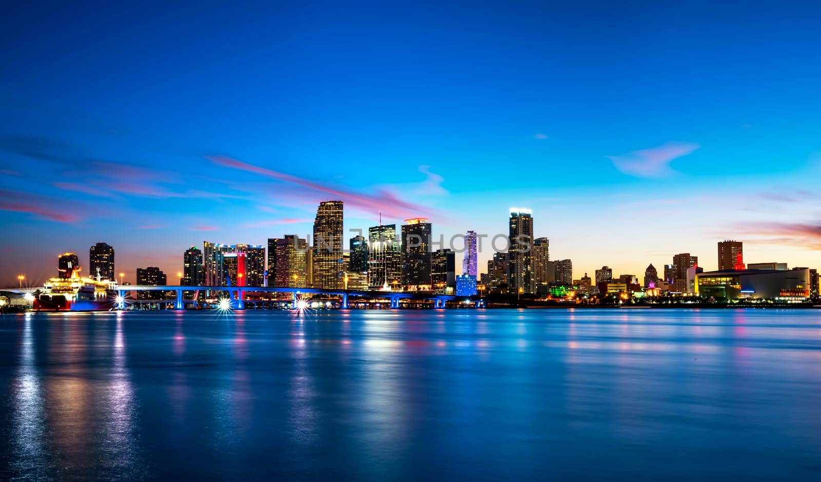 Miami city skyline panorama at dusk with urban skyscrapers over sea with reflection