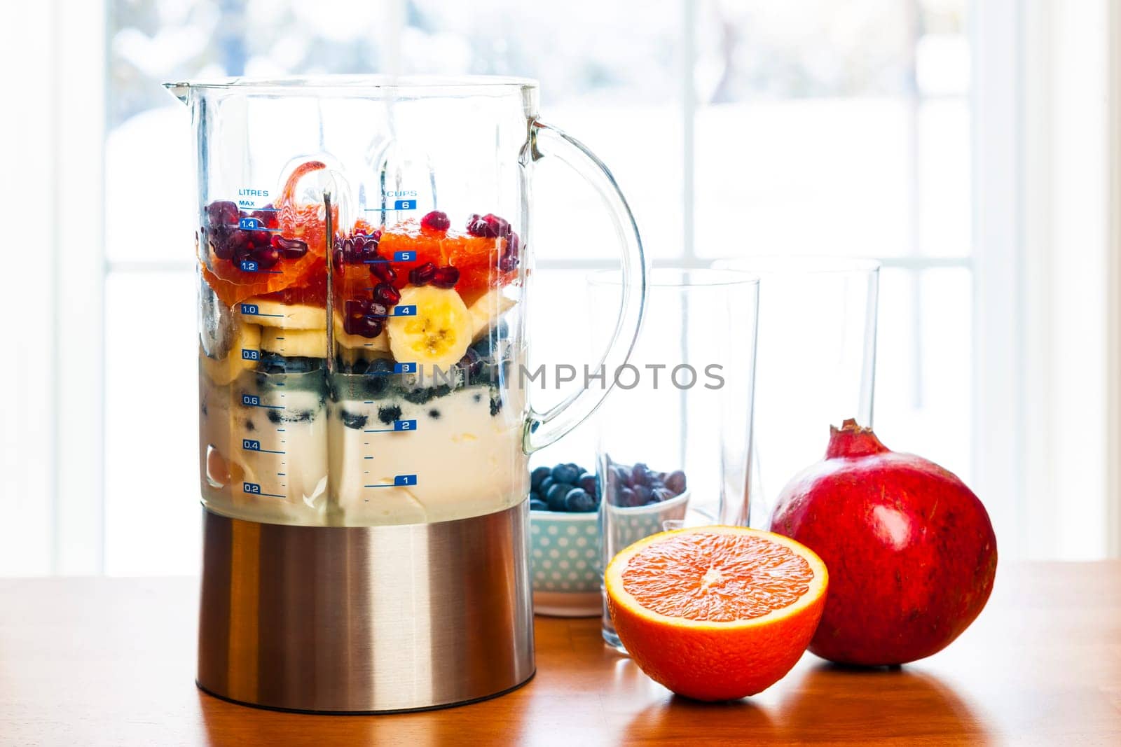 Healthy smoothie ingredients in blender with fresh fruit ready to blend on kitchen table