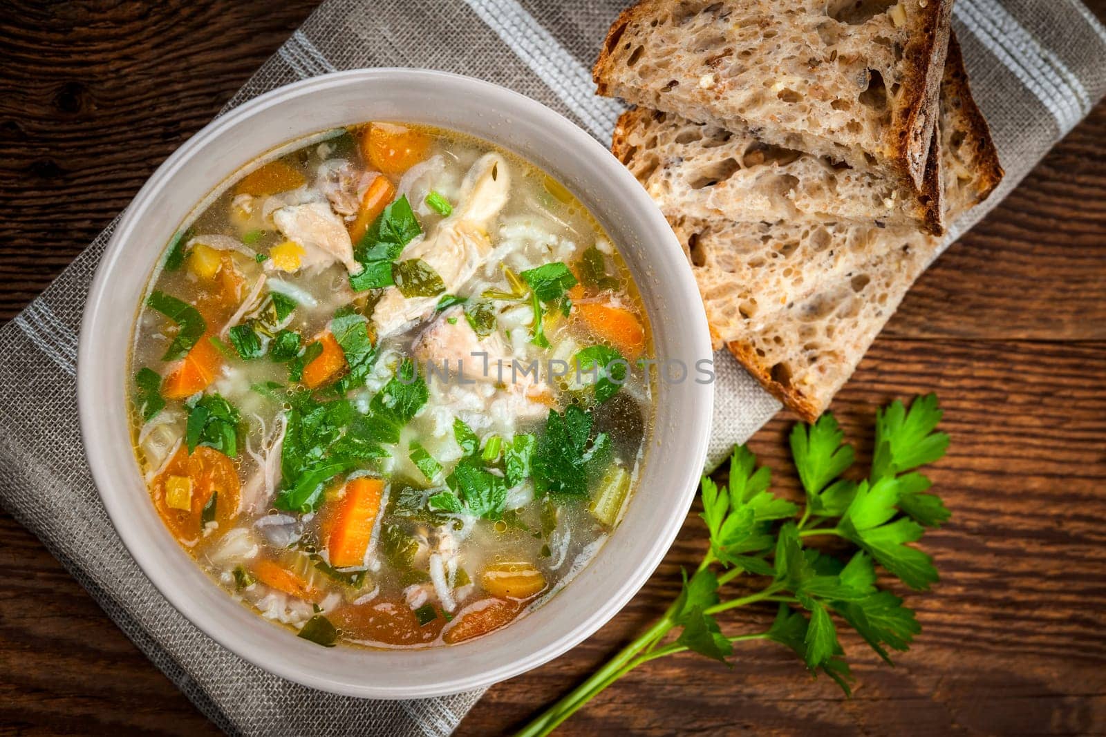 Chicken rice soup with vegetables in bowl and bread from above