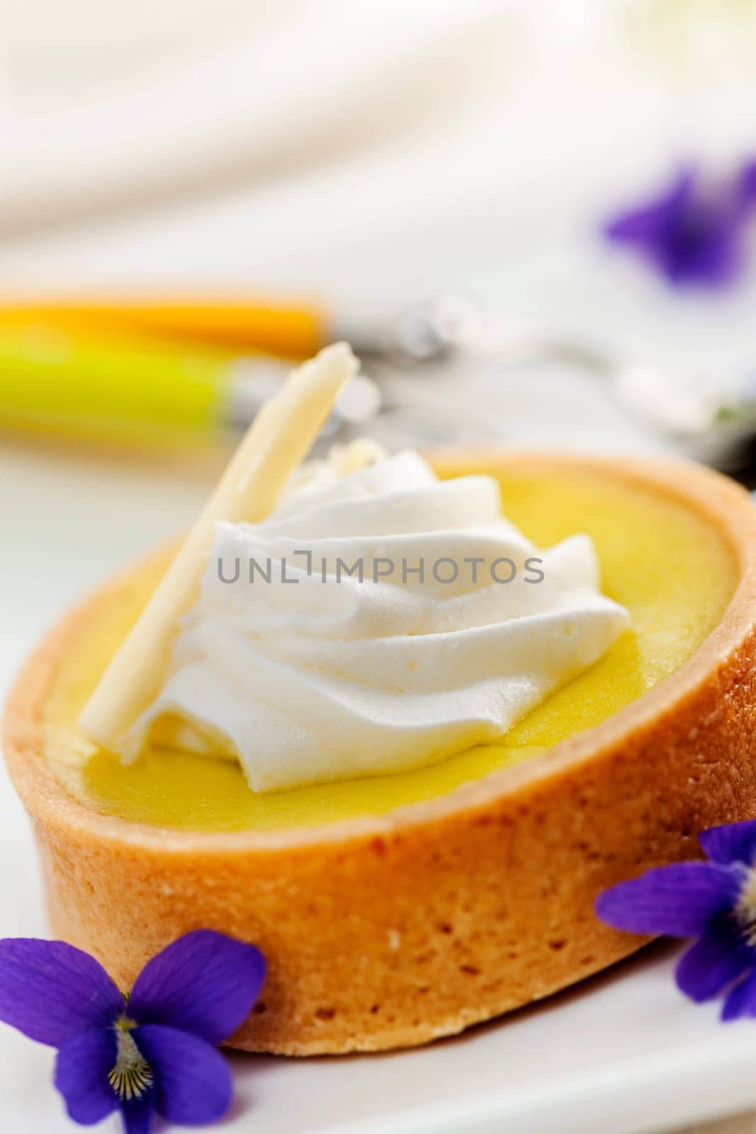 Fresh gourmet lemon dessert tart with edible violet flowers garnish
