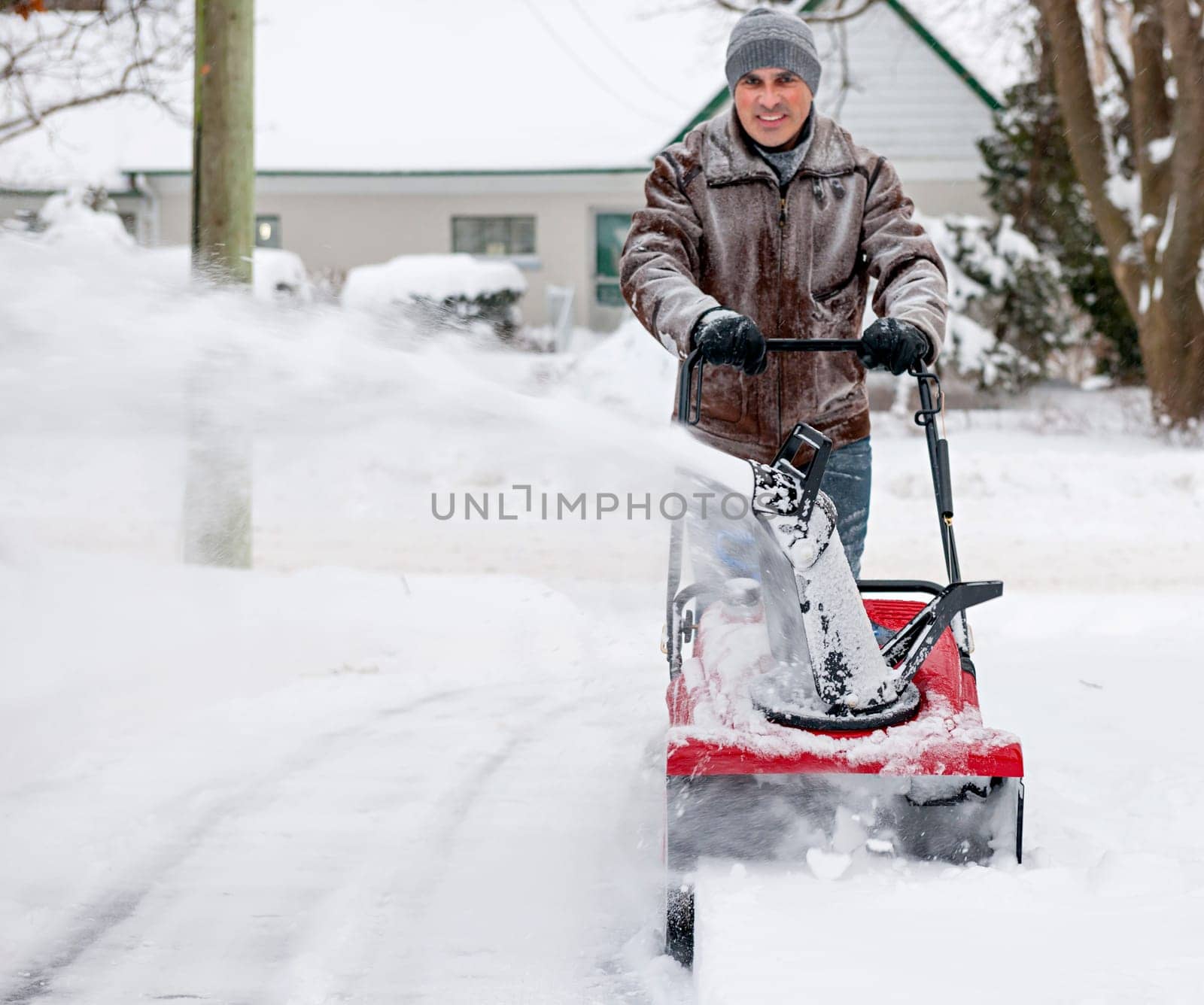 Man using snowblower to clear deep snow on residential driveway after heavy snowfall