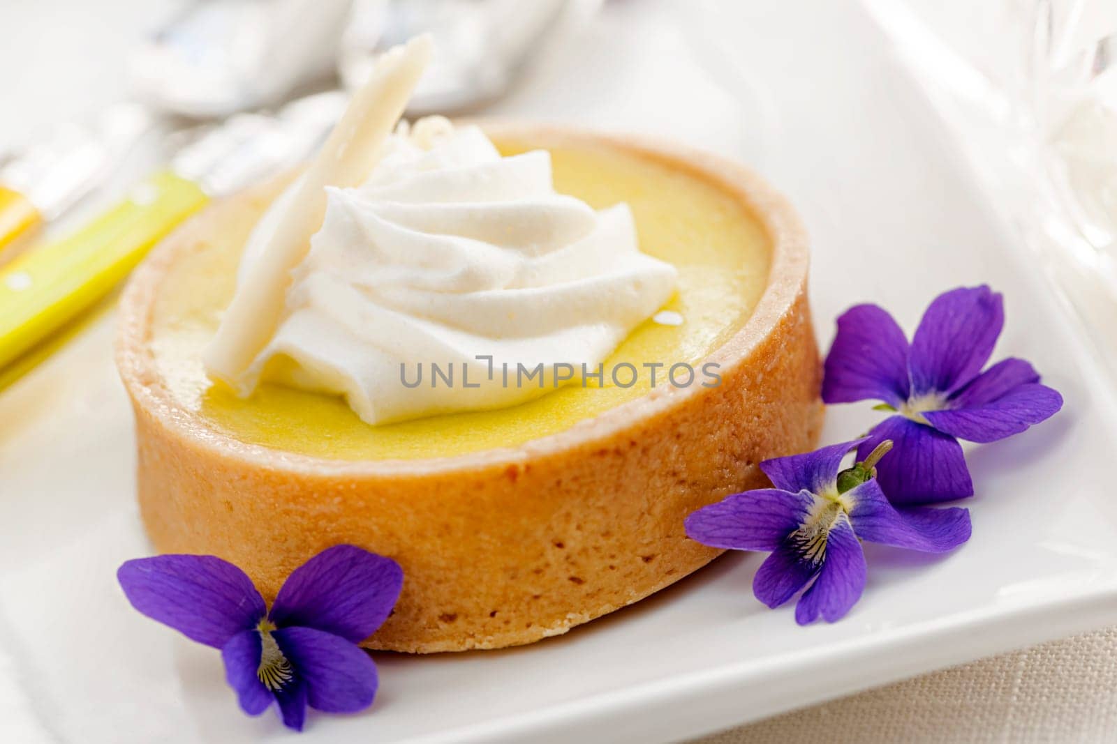 Fresh gourmet lemon dessert tart with edible violet flowers garnish