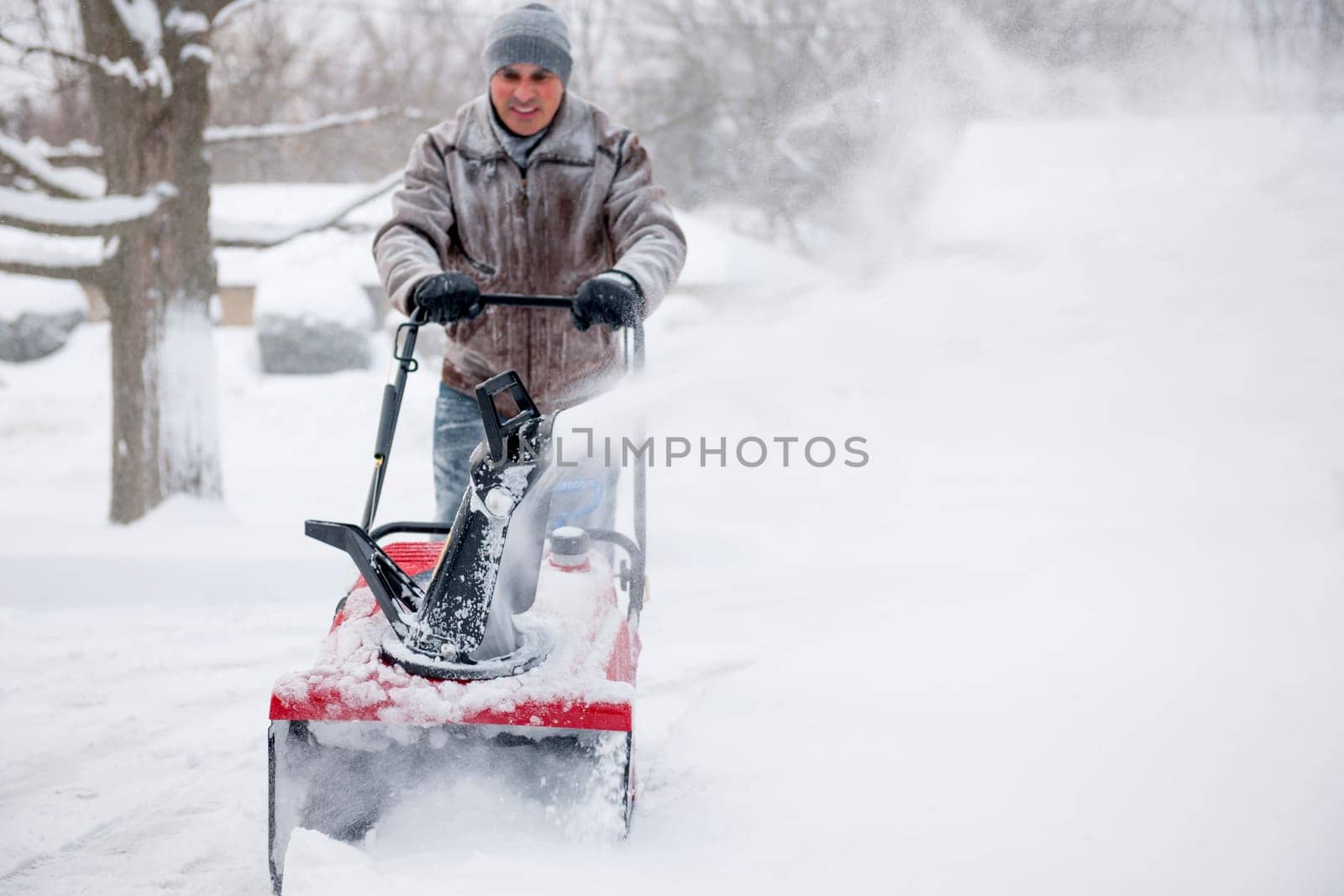 Man using snowblower to clear deep snow on residential driveway after heavy snowfall