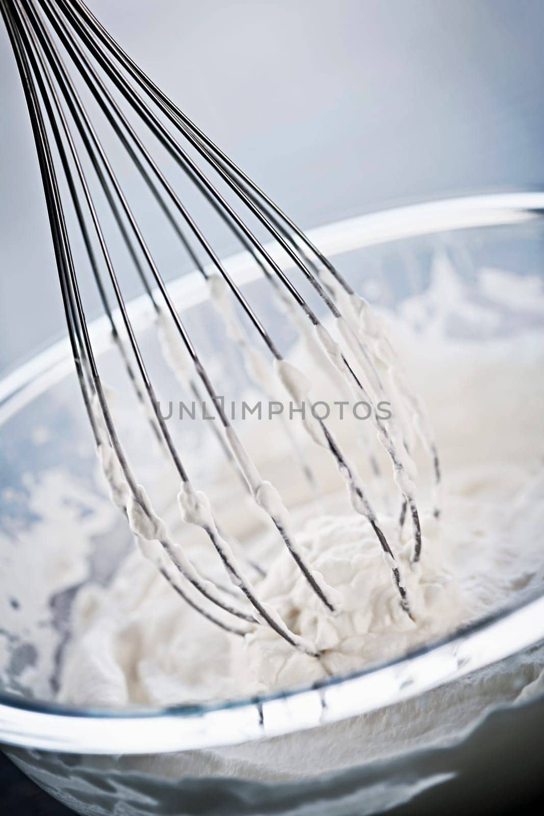 Closeup of metal whisk whipping cream in glass bowl