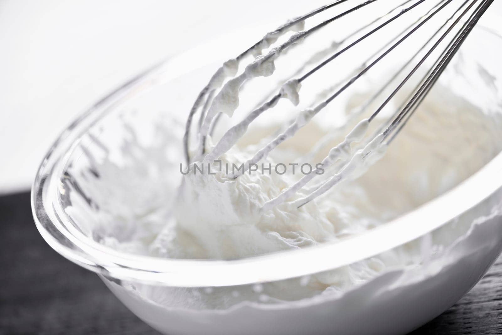 Closeup of metal whisk whipping cream in glass bowl