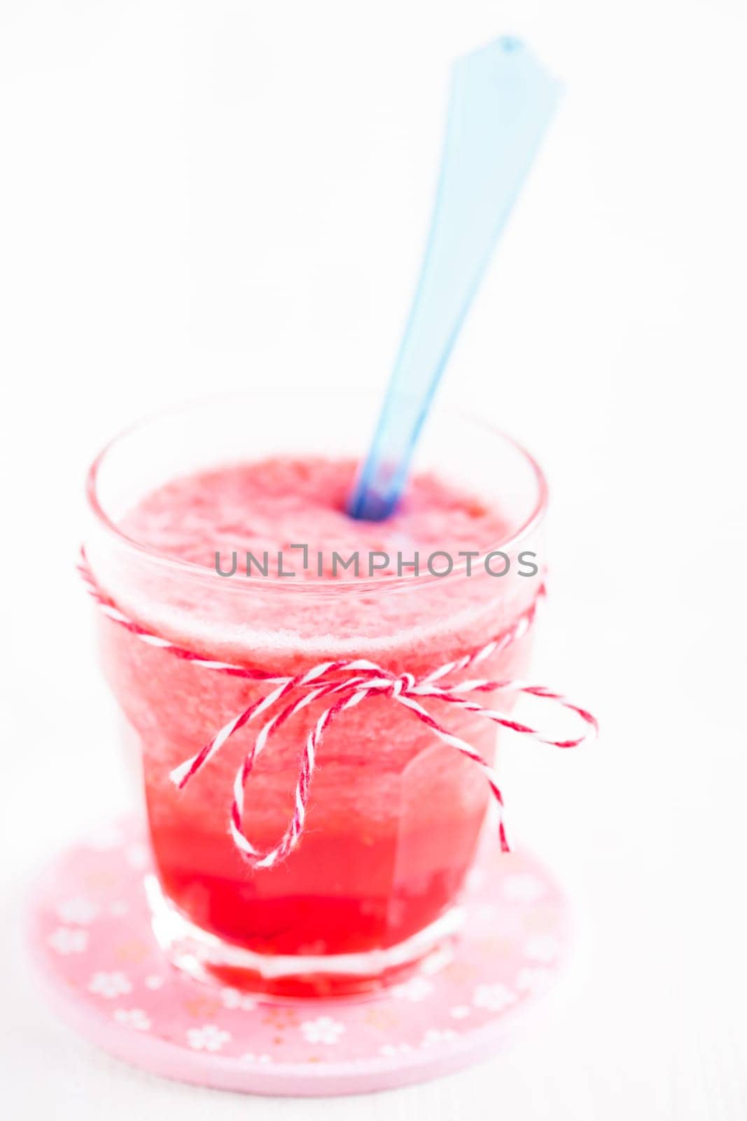 Closeup of strawberry smoothie and blue plastic spoon in glass on pink plate