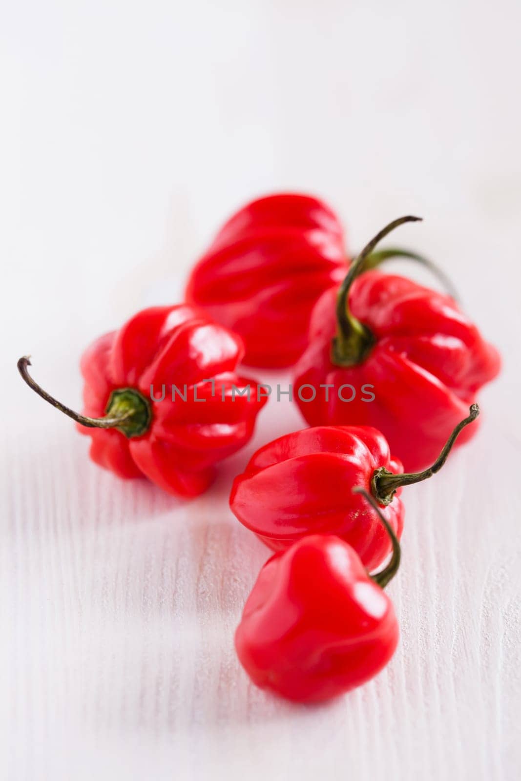 Closeup of bunch of five round shaped red chili peppers on light surface