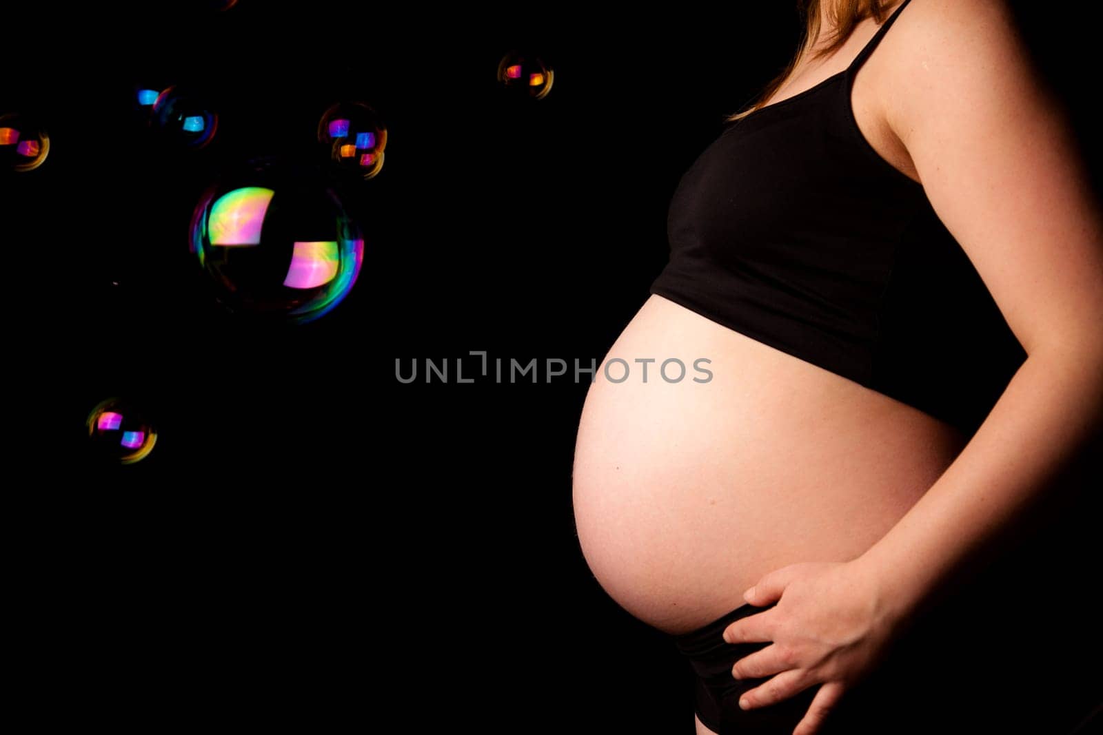 Belly of pregnant woman with soap bubbles. Monochrome and color mix. Black background
