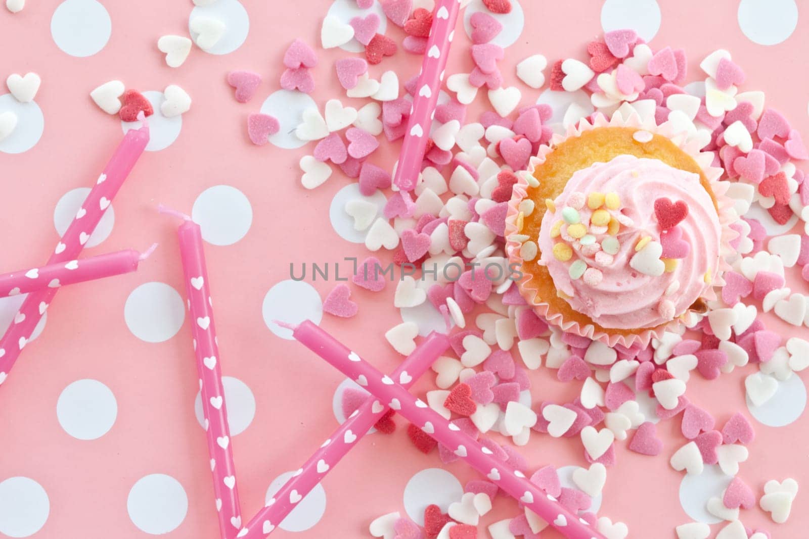 Small colorful cupcake with pink sprinkles in heart shape and birthday candles